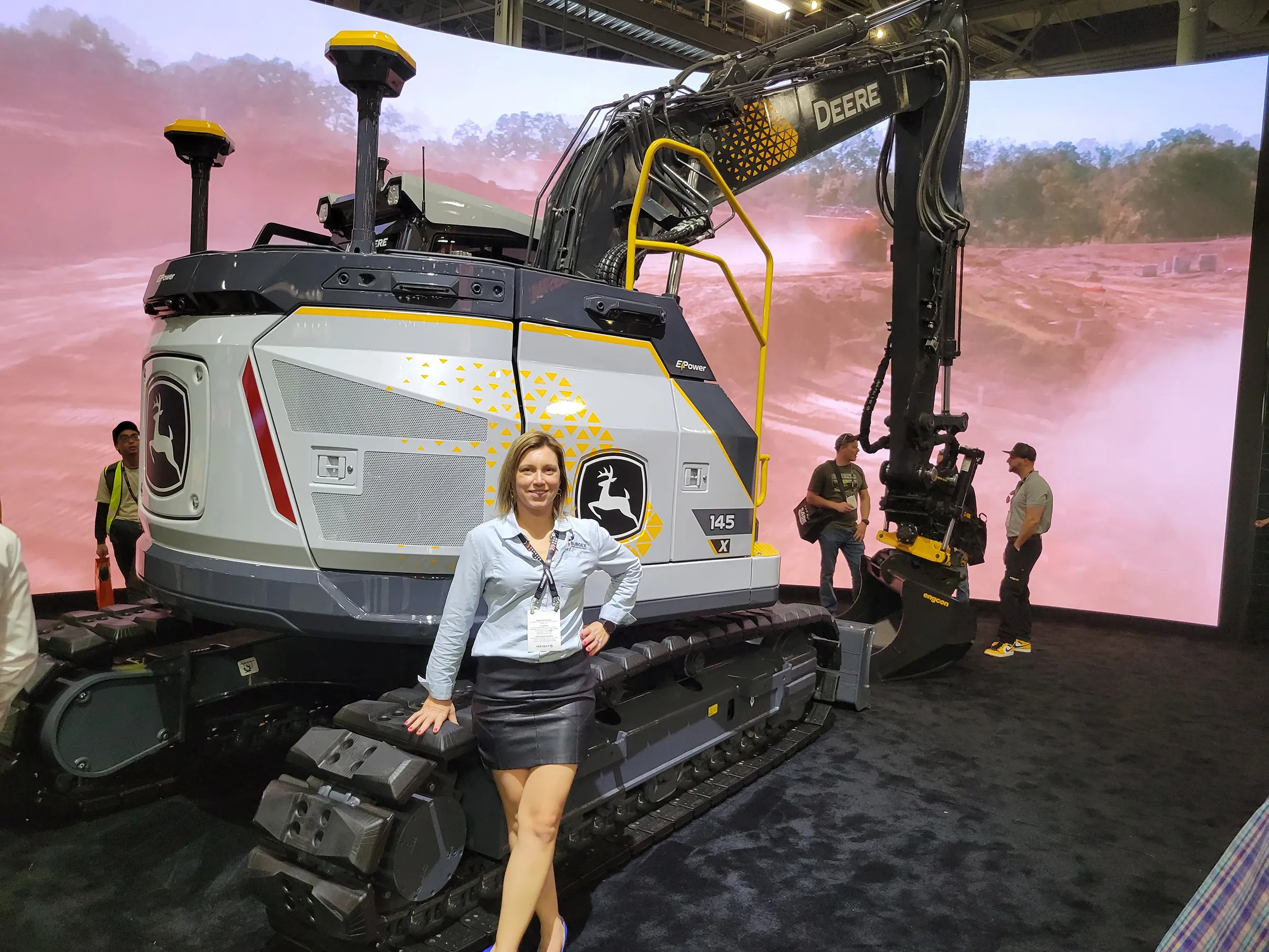 Amanda from Burgex stands next to an electric John Deer excavator.