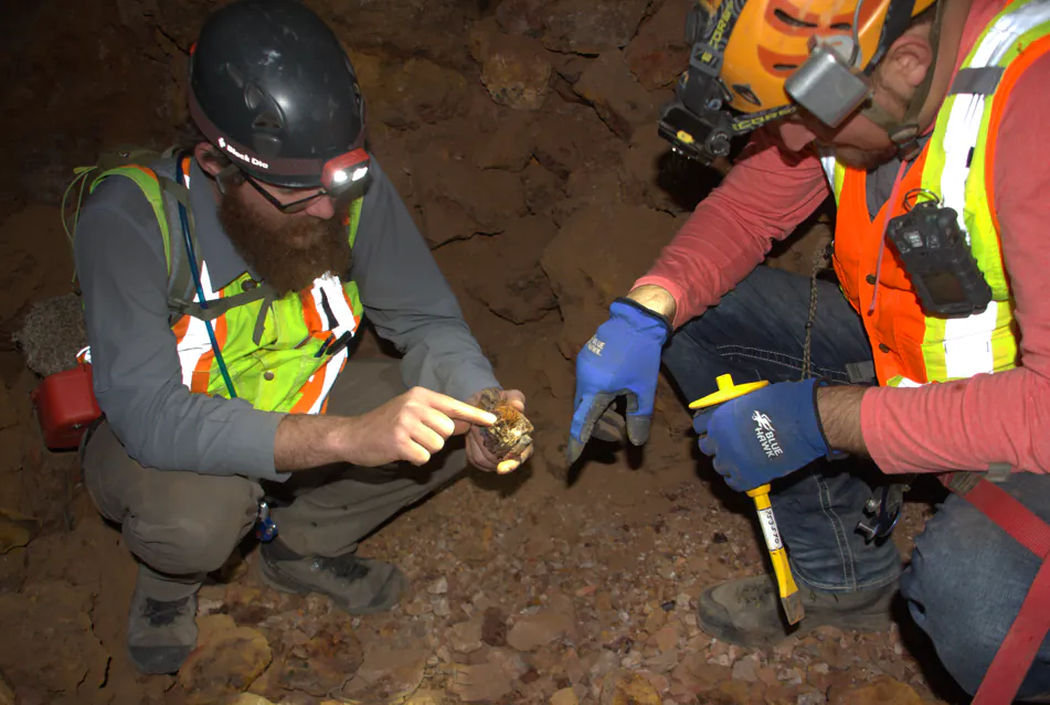 Two Burgex geologists in headlamps examining a rock core sample underground