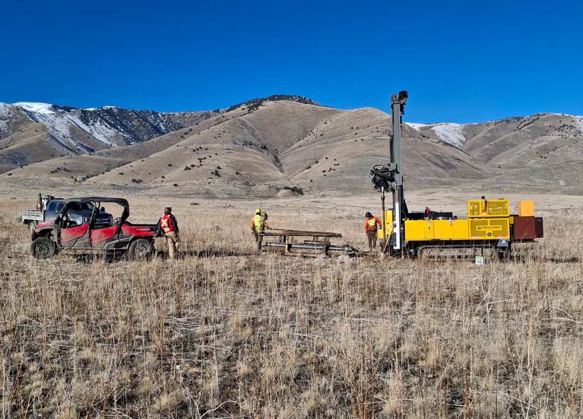 Drilling and exploration equipment on a desert hillside with mountains behind